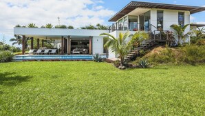 Una casa moderna de dos pisos con piscina, mobiliario exterior y una escalera que lleva al nivel superior.