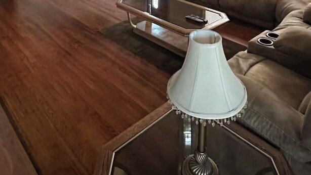 Un soggiorno con un divano in pelle marrone, un tavolino in vetro, una lampada bianca, una ventola a soffitto, un televisore a schermo piatto montato a parete e una porta con finestra.