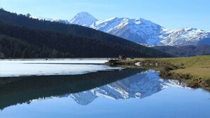 A serene lake with a clear reflection of snow-capped mountains, surrounded by a forested area. - To complete (Bagnères-de-Bigorre)