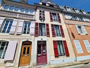 A multi-story building with distinct architectural features, including a variety of window styles and shutters, and a visible door with a number plaque.