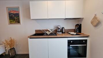 A compact kitchen with white cabinets, a coffee maker, a kettle, and a built-in oven.
