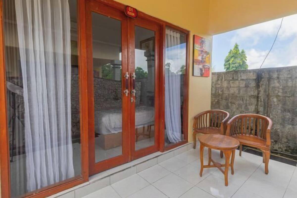 A room with a sliding glass door leading to a balcony, a bed, and two wooden chairs.