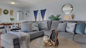 Un salon moderne avec un canapé d’angle, une table basse ronde et un petit panneau noir.