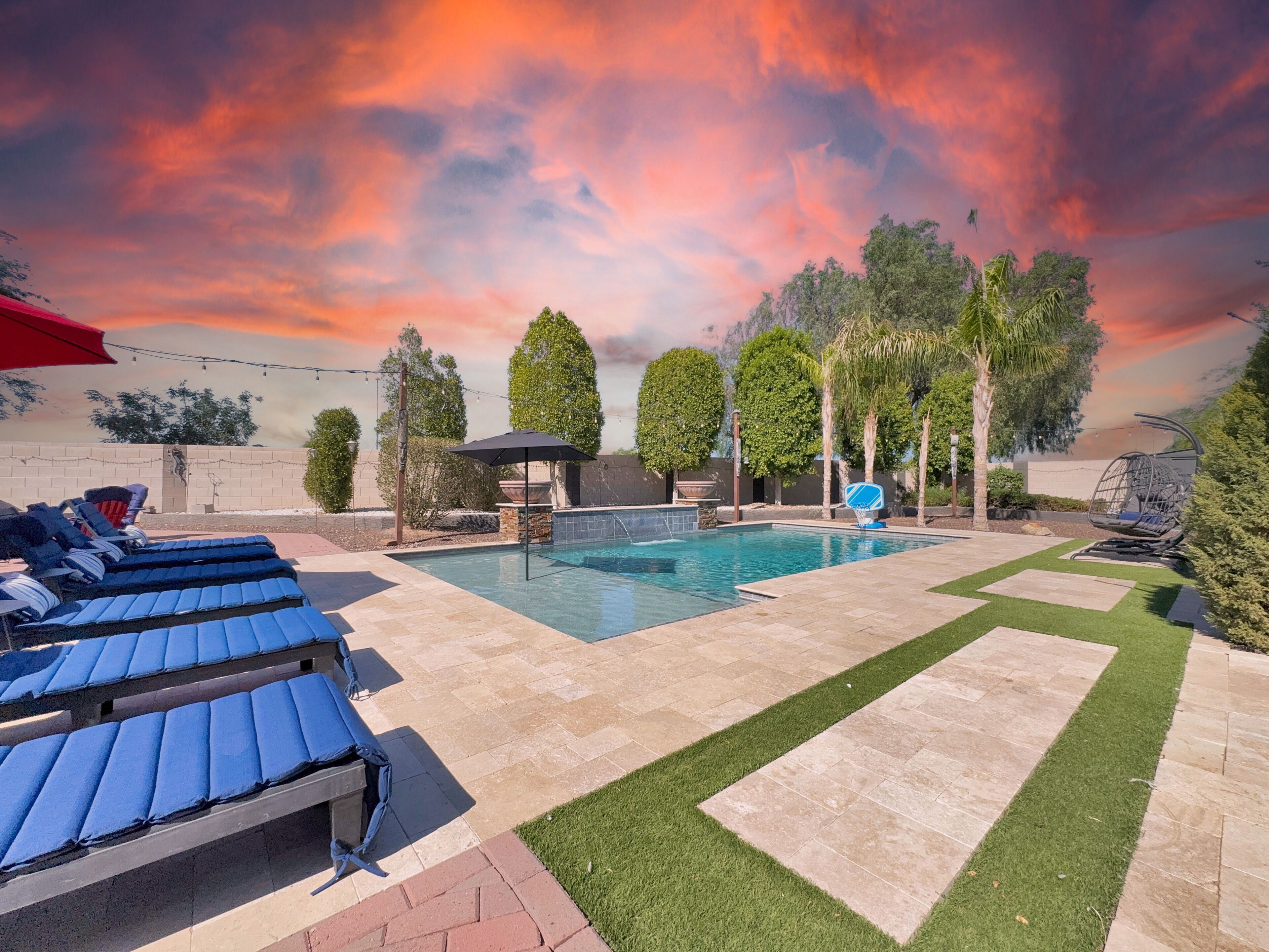 Ein Swimmingpool mit Liegestühlen, einem Grillbereich und Blick auf Bäume und einen Sonnenuntergang.
