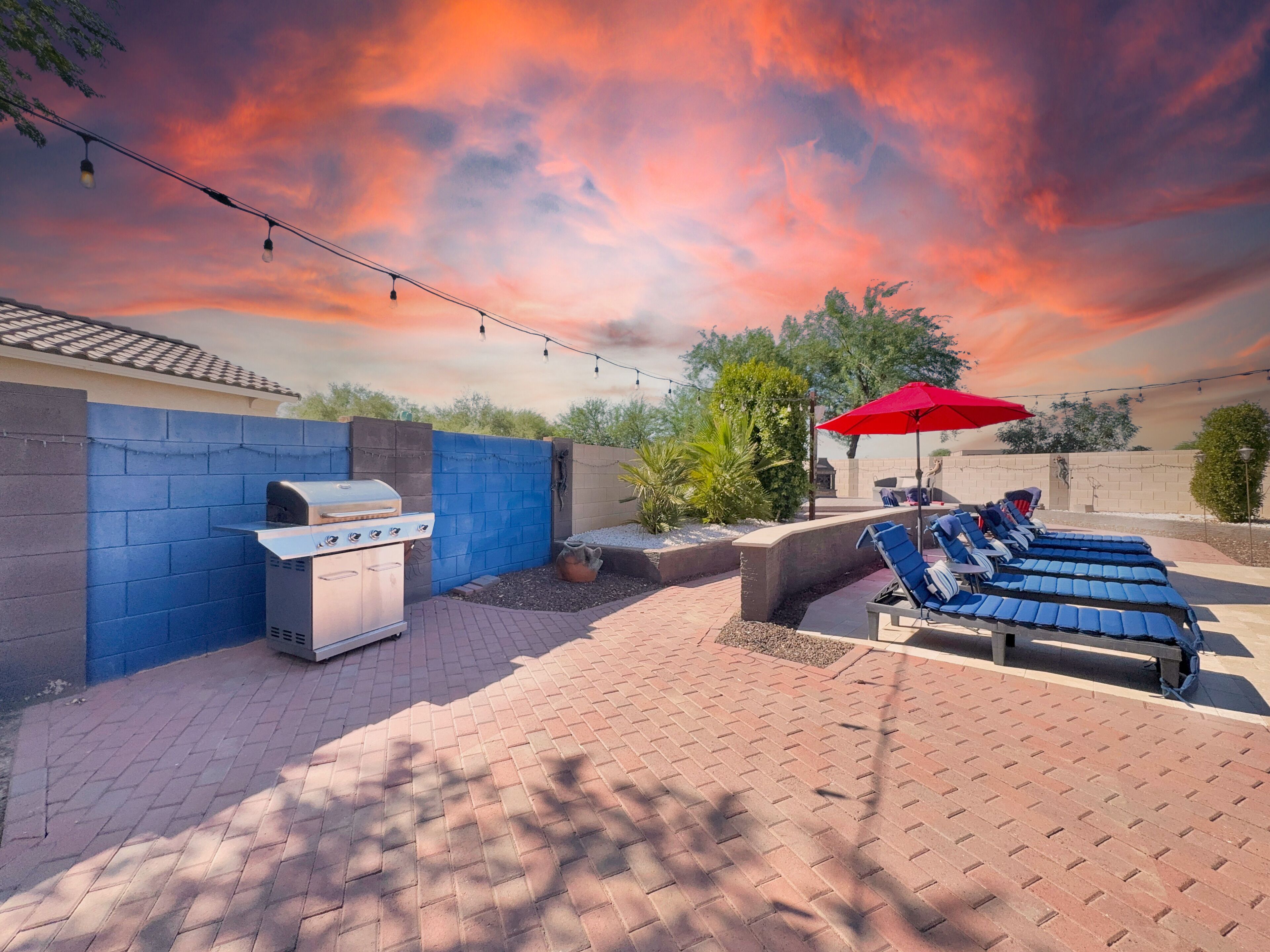 Eine Terrasse mit Grill, Liegestühlen und einem roten Sonnenschirm.