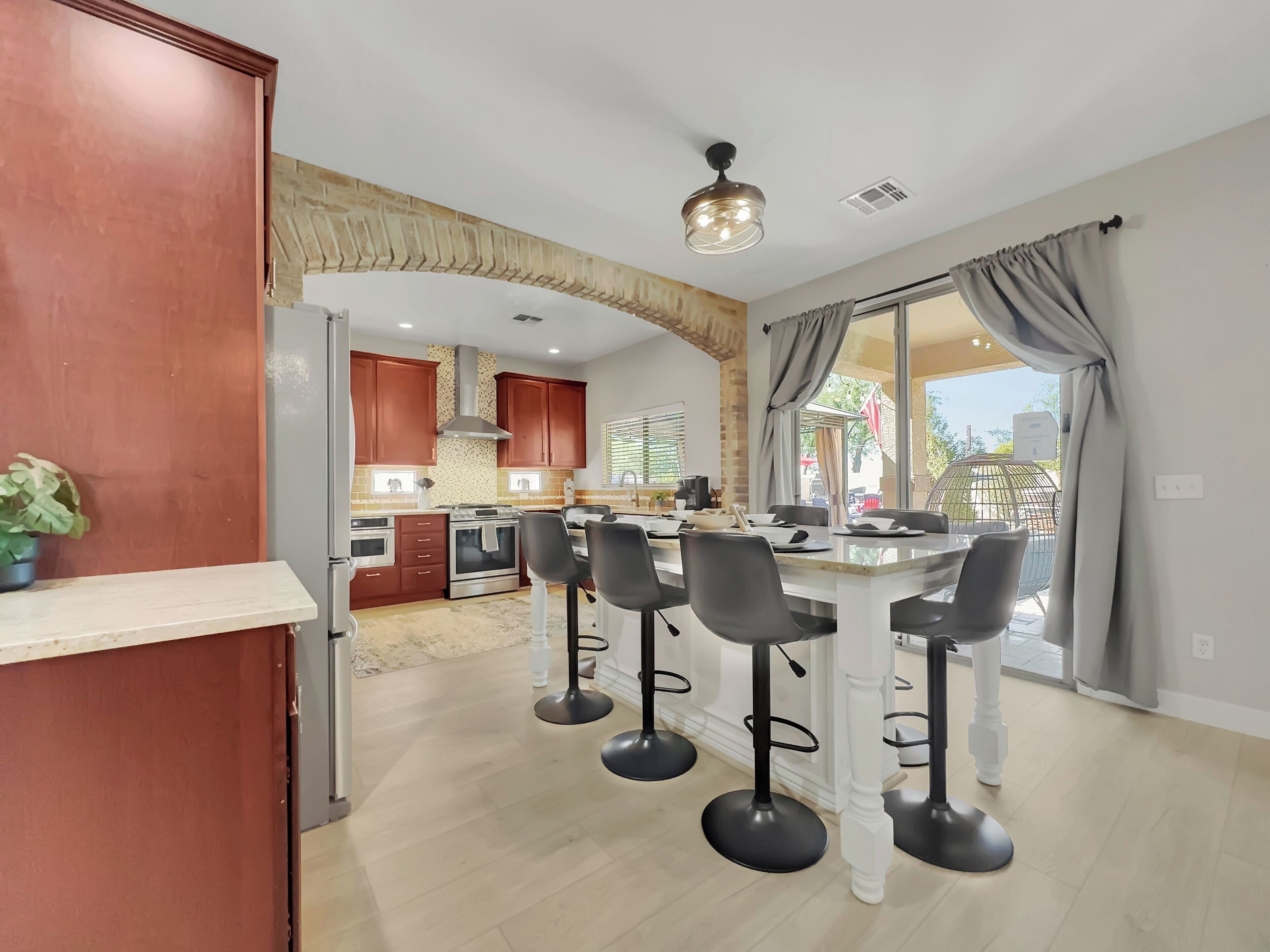 A modern kitchen with wooden cabinets, a central island with bar stools, and a view of the outdoors.