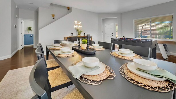 Un comedor moderno con una mesa larga preparada para una comida, una mesa de fútbol de mesa y una escalera que lleva a otro nivel.