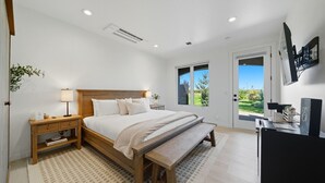 A bedroom with a wooden bed, bedside tables, a desk, and a view of the outdoors.