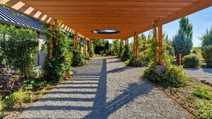 A covered walkway with a gravel path, wooden columns, and greenery.