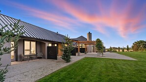 Une maison moderne dotée d’un grand patio, d’un espace salon extérieur abrité et d’une pelouse bien entretenue.