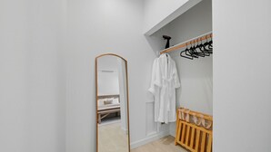 Une pièce avec un grand miroir, un berceau en bois, un portant à vêtements et un lit avec une tête de lit.
