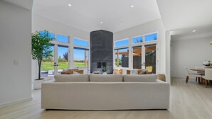 Ein geräumiges Wohnzimmer mit einer großen Couch, einem Kamin und bodengrossen Fenstern mit Blick ins Freie.