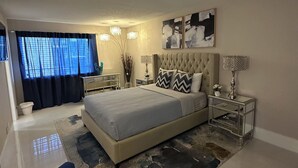 Un dormitorio moderno con una cama grande, un sofá azul, una mesita de noche y un ventanal con cortinas.
