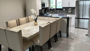 Una cocina moderna con armarios blancos, un refrigerador de acero inoxidable y un comedor con mesa de mármol y sillas tapizadas.