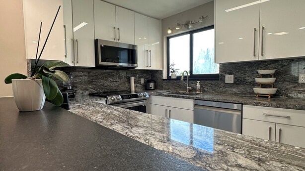 Una cocina moderna con gabinetes blancos, encimera de granito y microondas integrado.