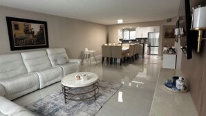 Una sala de estar moderna con un sofá de cuero blanco, una mesa de centro redonda y un comedor con una mesa y sillas blancas.