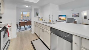 Una cocina moderna con muebles blancos, lavavajillas y un comedor con mesa y sillas.