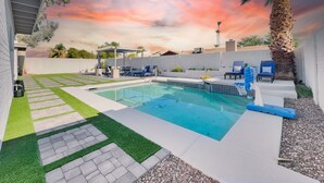 Una piscina con pérgola, sillas de descanso y una palmera.