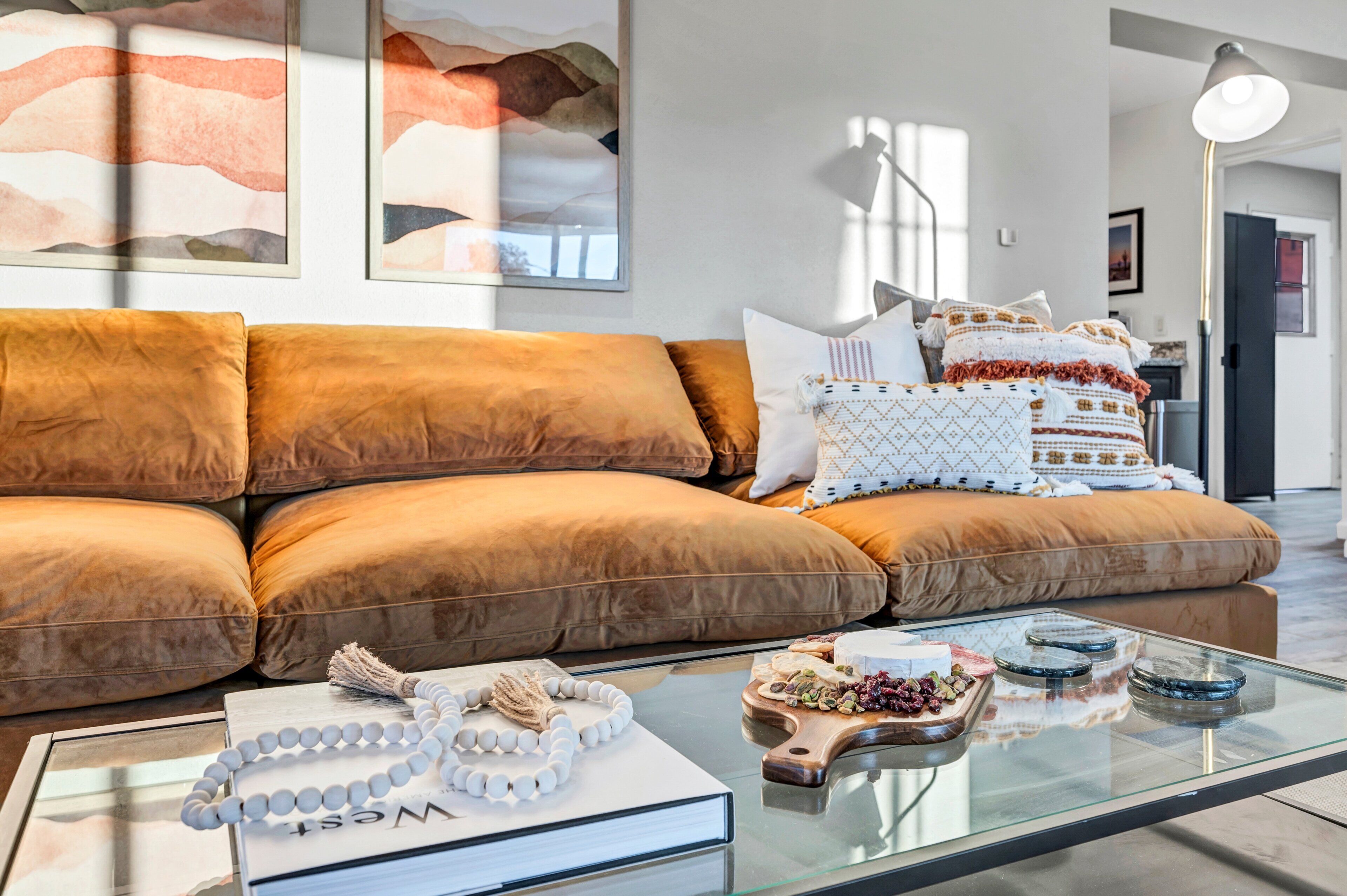 A modern living room with a brown sofa, a glass coffee table with decorative items, and a bookshelf.