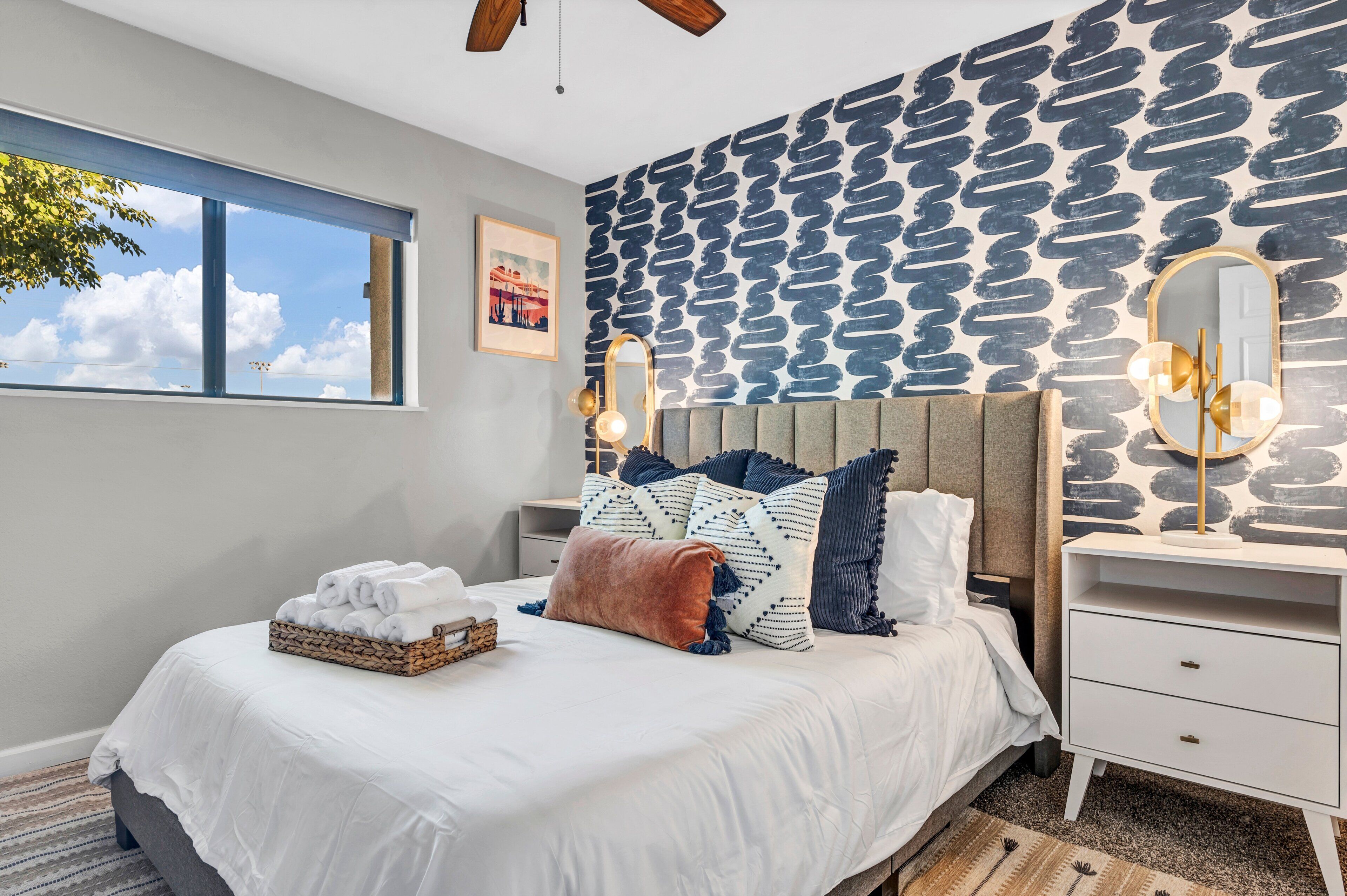 A bedroom with a bed, a bedside table, a nightstand, a window, and a wall with a patterned design.