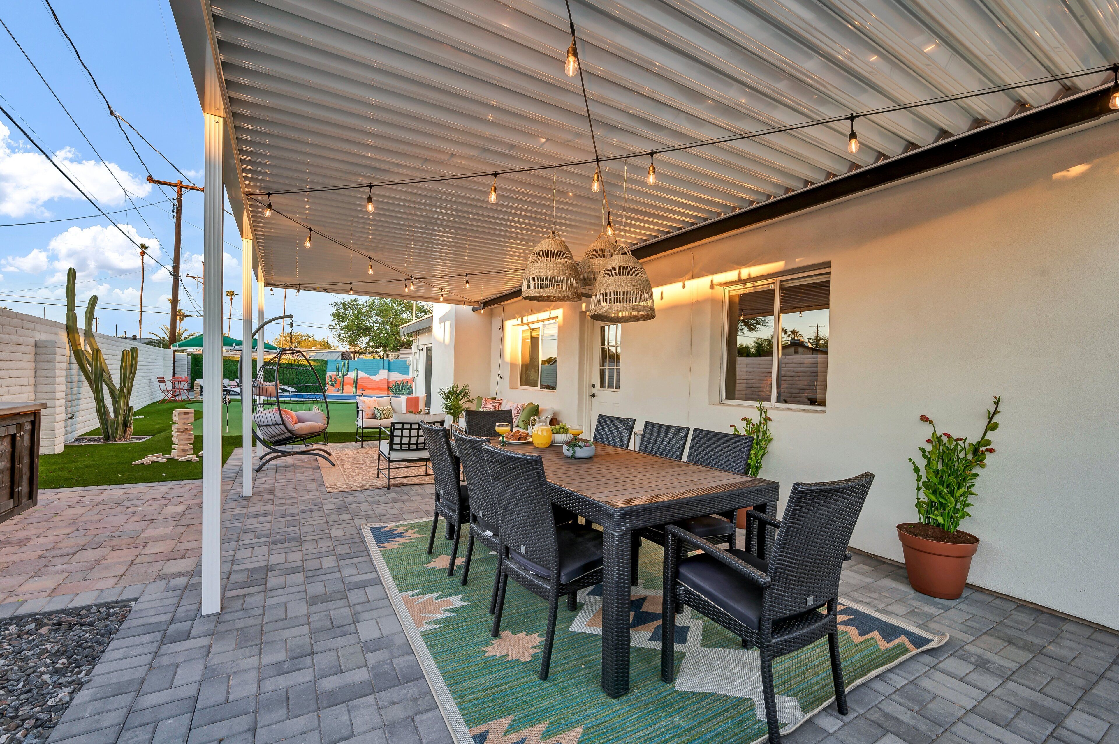 An outdoor patio with a covered dining area, wicker chairs, a table set with plates and a pitcher, and potted plants.