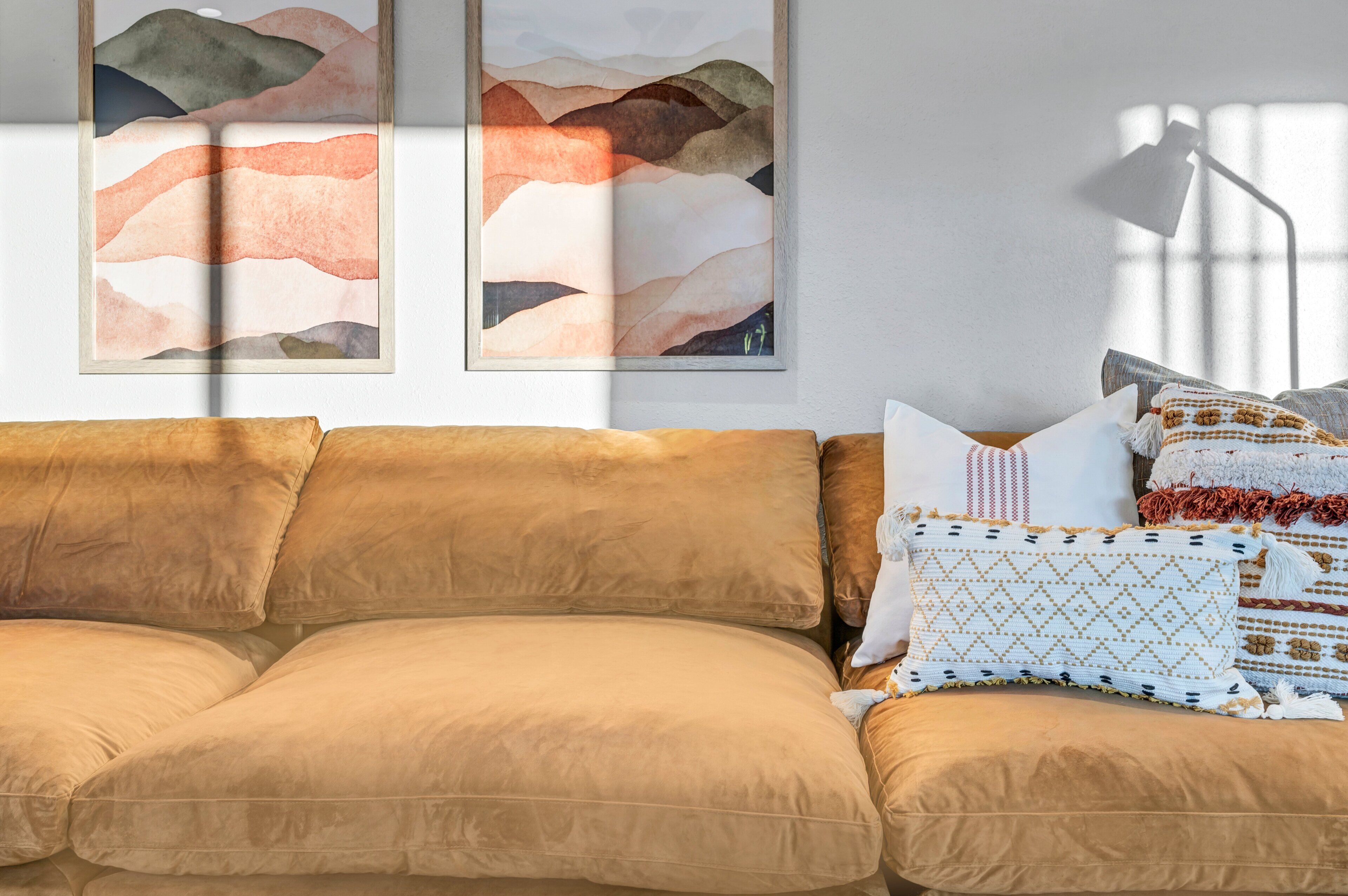 A cozy living room with a brown sofa, patterned cushions, and abstract wall art.