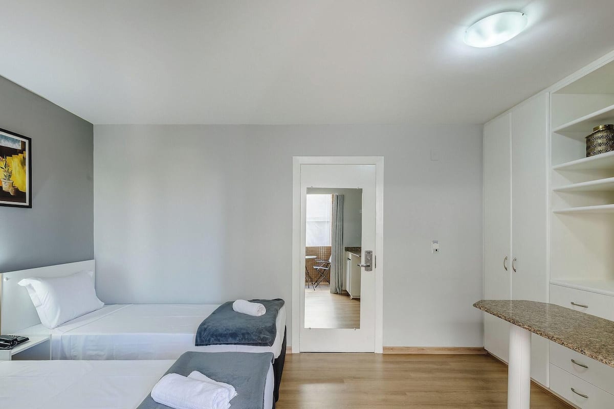 Een hotelkamer met twee bedden, een kleine kitchenette, een spiegel en een deur naar een badkamer.