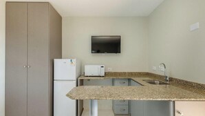 A compact kitchen with a microwave, a sink, and a flat-screen TV mounted on the wall. - Studios at Upper Residence - UPP (Curitiba)