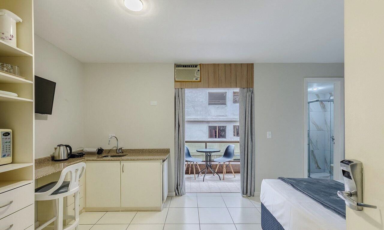 A compact hotel room with a kitchenette, a small dining area, and a bathroom with a glass shower.