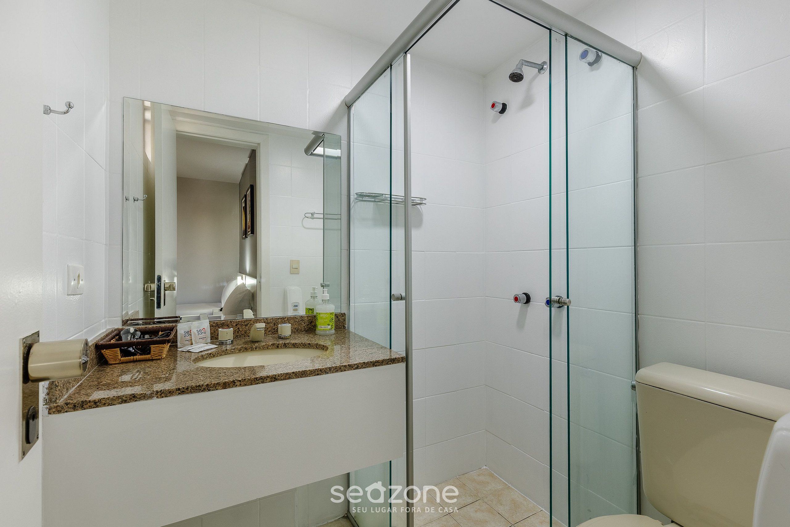 Een badkamer met een douchecabine van glas, een wastafel met een granieten aanrechtblad en een toilet.