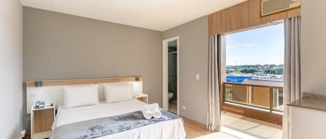 Un dormitorio con cama, mesitas de noche, puerta de baño y balcón con vistas.