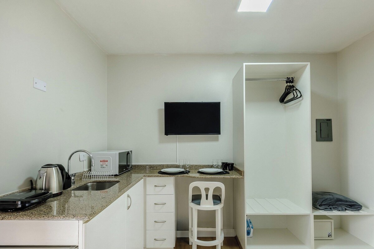 Une petite cuisine équipée d’un four à micro-ondes, d’une bouilloire et d’un grille-pain. Un téléviseur à écran plat est fixé au mur, et un petit coin salon avec une chaise est à disposition.