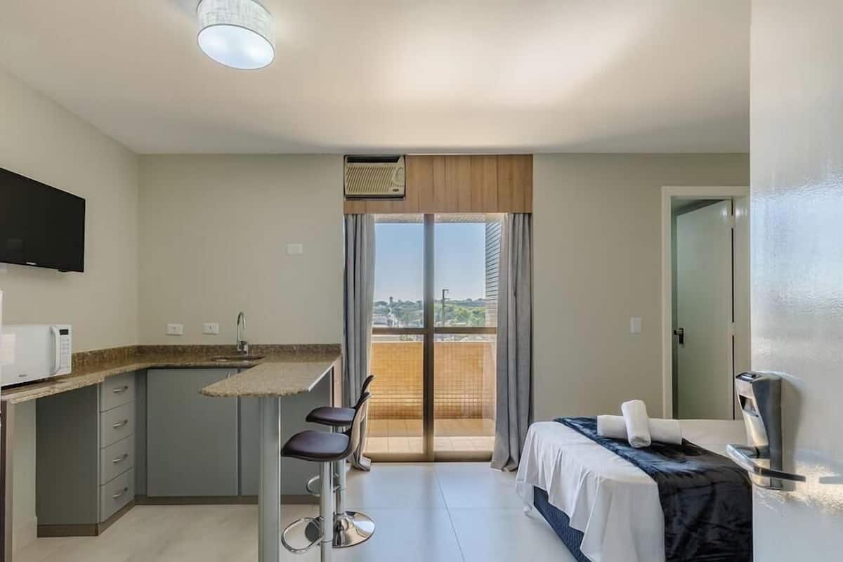 Een compacte hotelkamer met kitchenette, een bed, een televisie en een balkon met uitzicht.