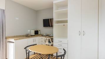 A compact kitchen with a microwave, white cabinets, a small table, and a TV mounted on the wall.