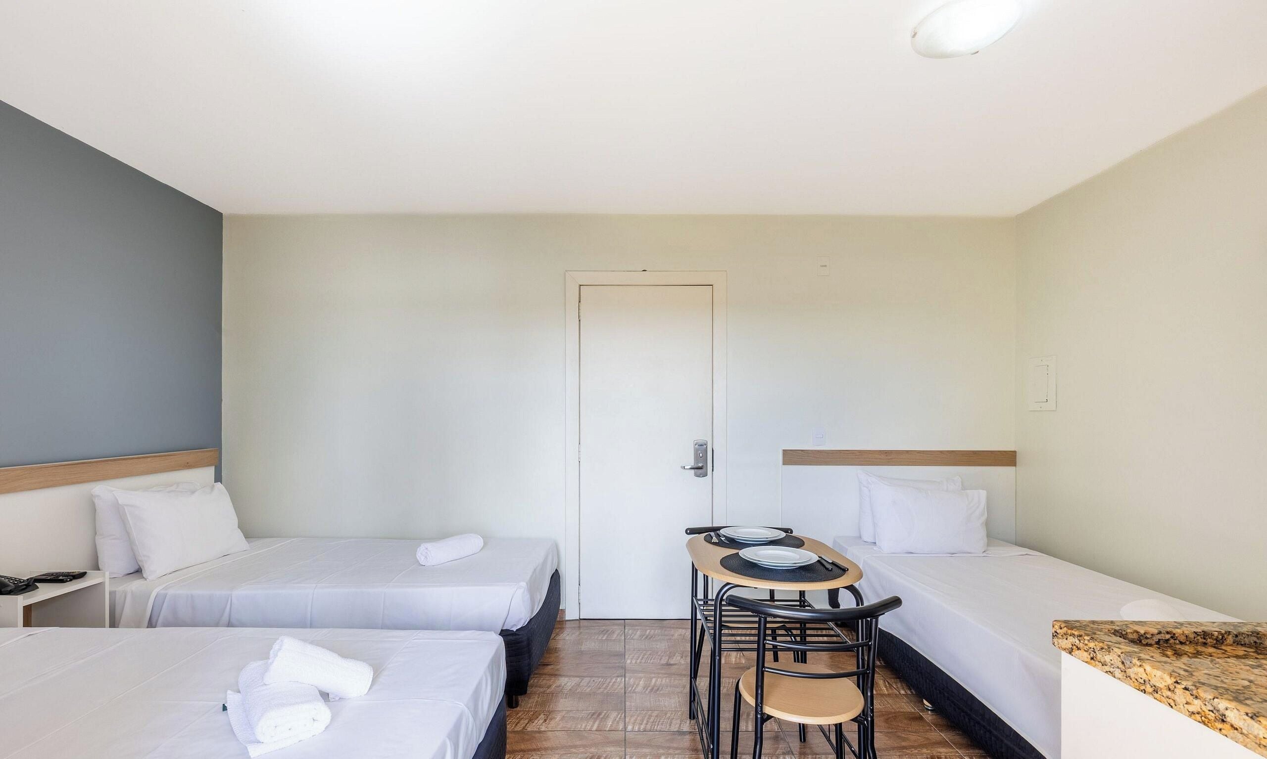 Una habitación de hotel con dos camas individuales, una mesita con sillas y una puerta.