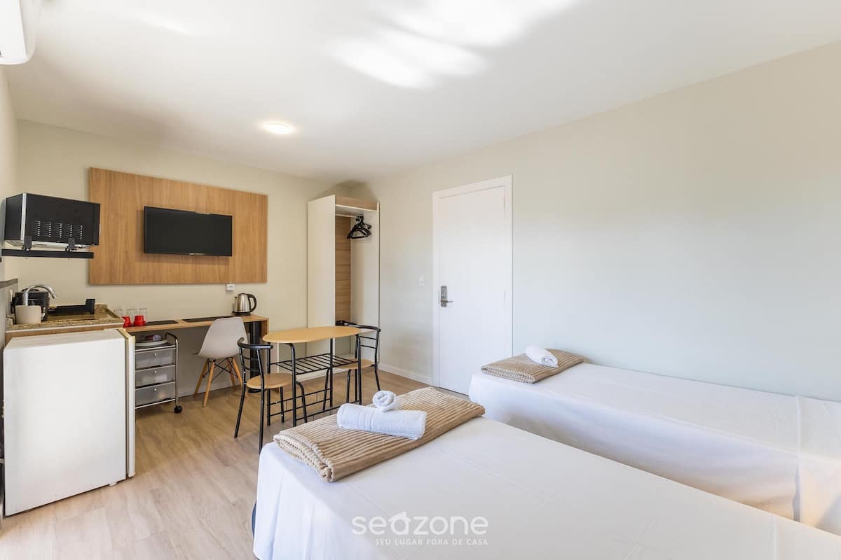 Een kleine hotelkamer met kitchenette, een enkel bed, een bureau met stoel en een aan de muur bevestigde televisie.