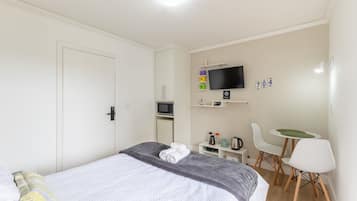 A bedroom with a bed, a TV, a desk, and a chair.
