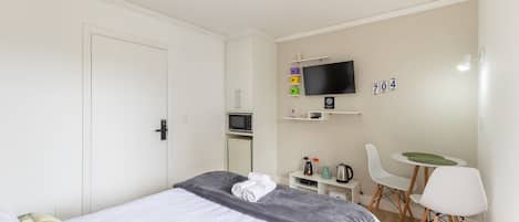 A bedroom with a bed, a TV, a desk, and a chair.