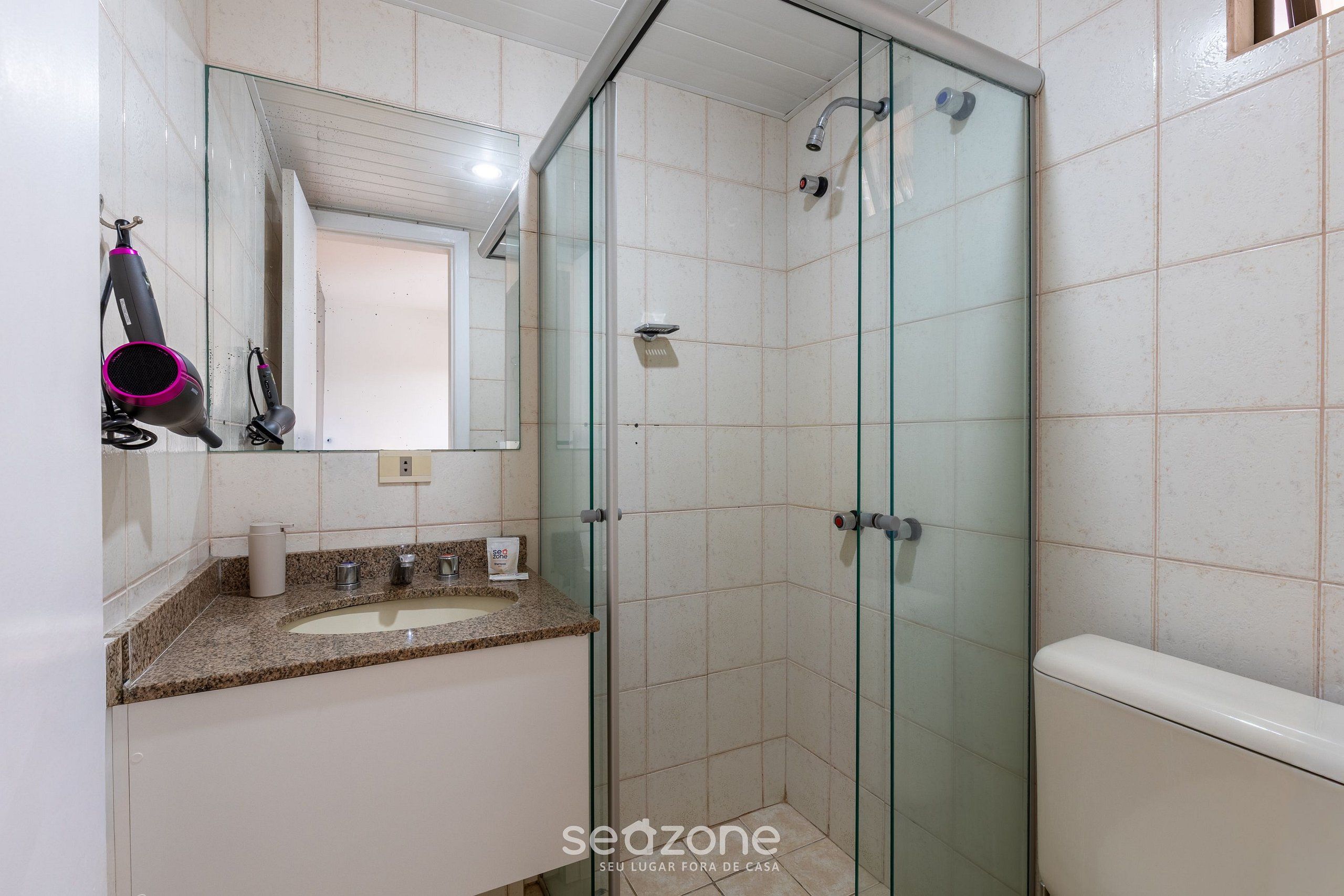 Een badkamer met een douchecabine van glas, een wastafel met een granieten aanrechtblad en een spiegel boven de wastafel.