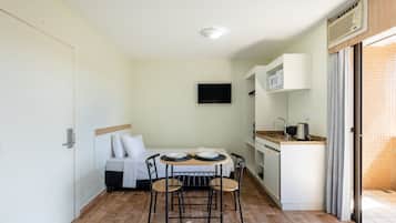 Una habitación compacta con cama, una pequeña mesa de comedor con sillas, un televisor montado en la pared y una kitchenette.