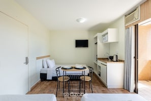 Una habitación compacta con cama, una pequeña mesa de comedor con sillas, un televisor montado en la pared y una kitchenette.