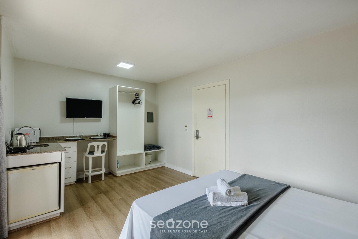A compact hotel room with a bed, a small kitchenette, a TV, and a wardrobe.