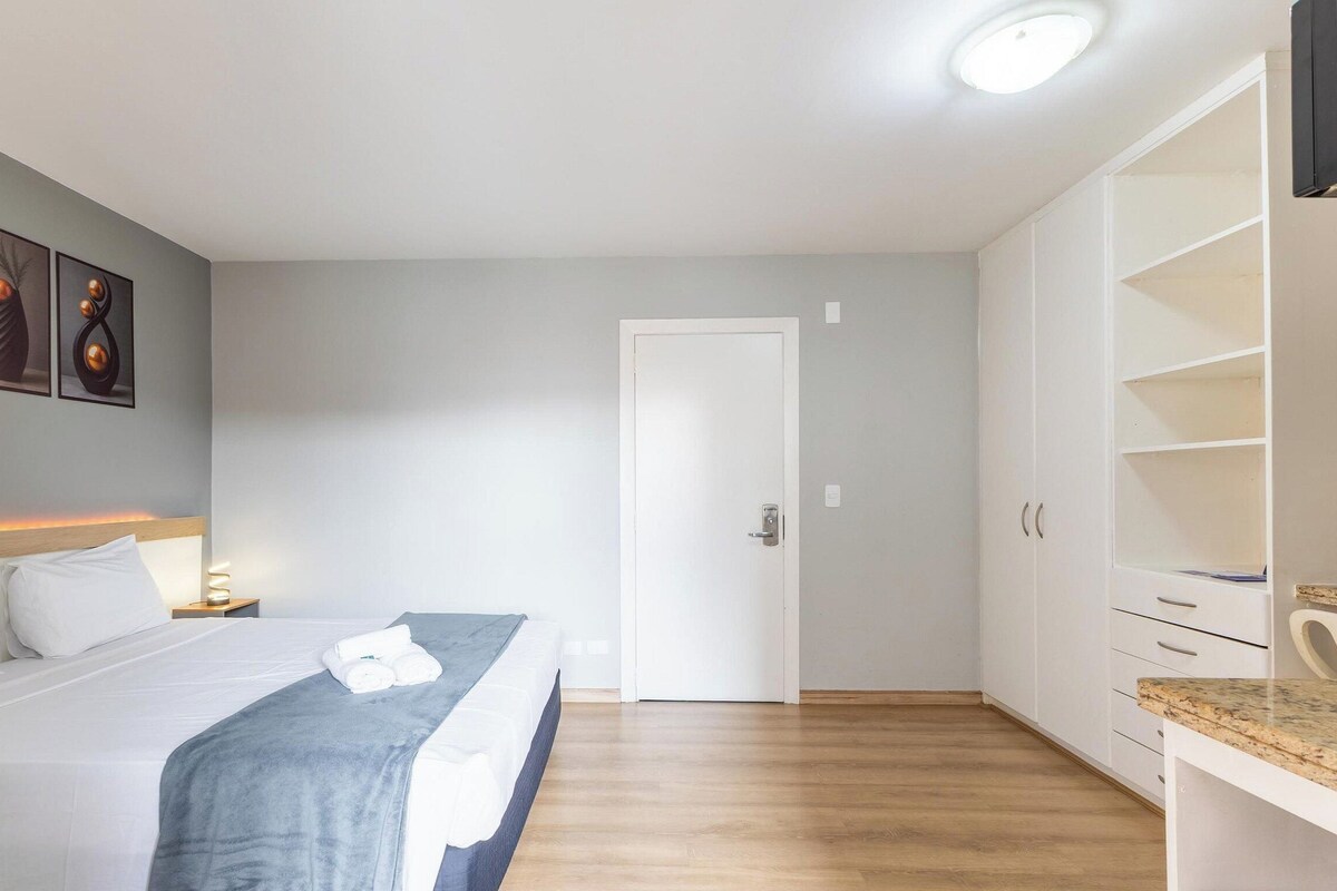 Una habitación de hotel con cama, mesita de noche, lámpara y armario.