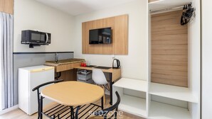 A compact kitchenette with a microwave, a small refrigerator, a wooden desk, a chair, and a TV mounted on the wall. - Studios at Upper Residence - UPP (Curitiba)