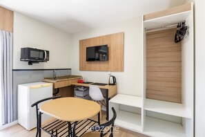 A compact kitchenette with a microwave, a small refrigerator, a wooden desk, a chair, and a TV mounted on the wall. - Studios at Upper Residence - UPP (Curitiba)