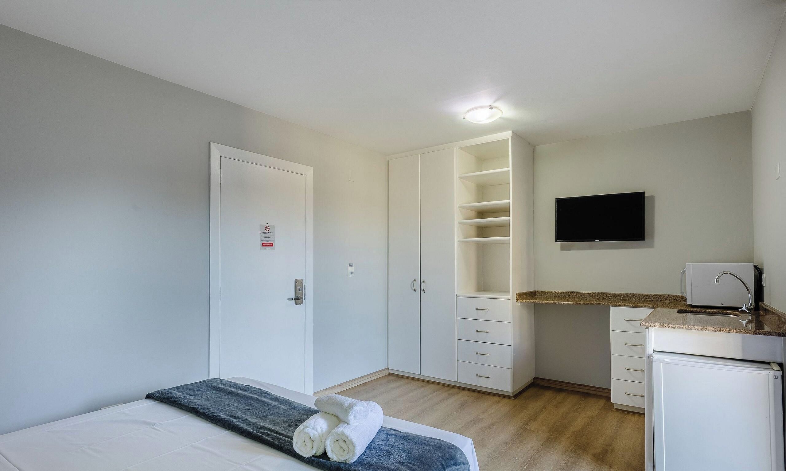 Une chambre avec un lit, une armoire, un téléviseur intégré et un coin cuisine.