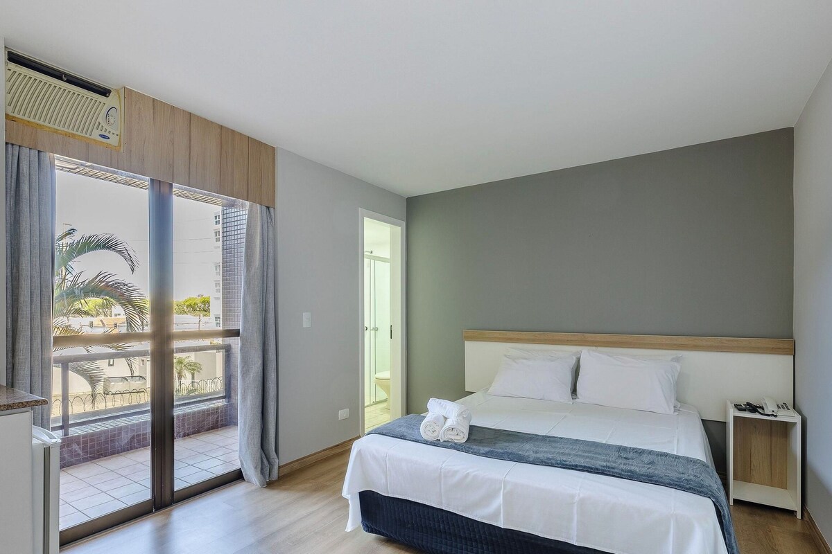 Una camera d'albergo con un letto, un comodino, una porta del bagno e vista sull'esterno.