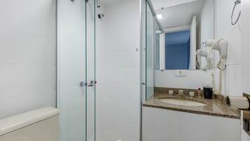 Casa de banho com cabine de chuveiro em vidro, lavatório com bancada de granito e secador de cabelo fixado na parede.