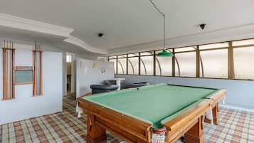 A pool table in a room with a checkered floor, a green ceiling light, and a view through large windows.