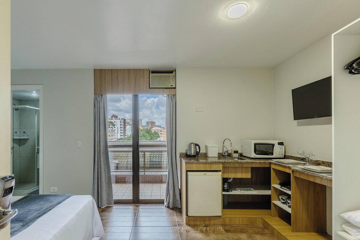 Een compacte hotelkamer met balkon, kitchenette, bed en douche.
